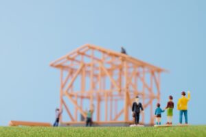 Toy construction site scene with an orange steel framework in the background and miniature workers standing on a grassy surface under a blue sky.