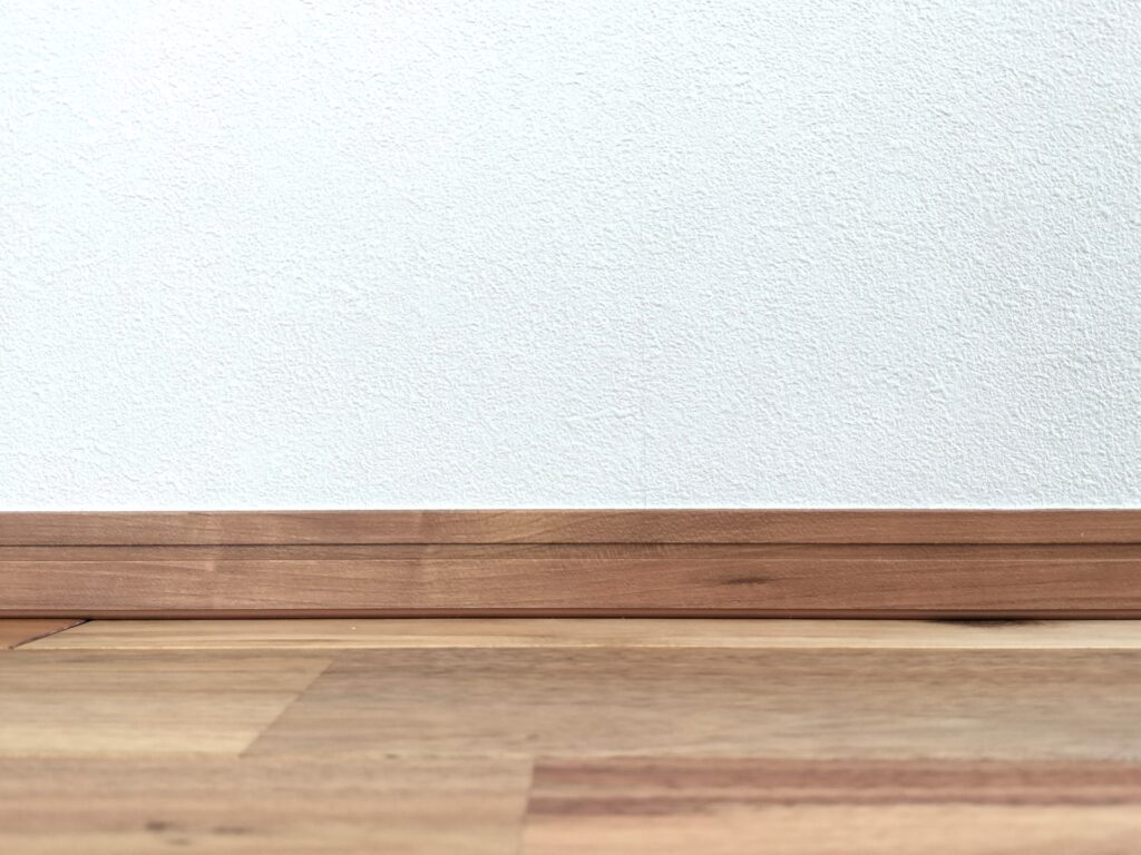 White textured wall with a brown wooden baseboard and floor, empty interior scene.