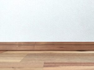 White textured wall with a brown wooden baseboard and floor, empty interior scene.