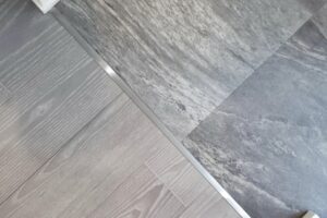Floor transition between light wood planks on the left and gray stone tiles on the right, with a metal threshold strip in the middle.