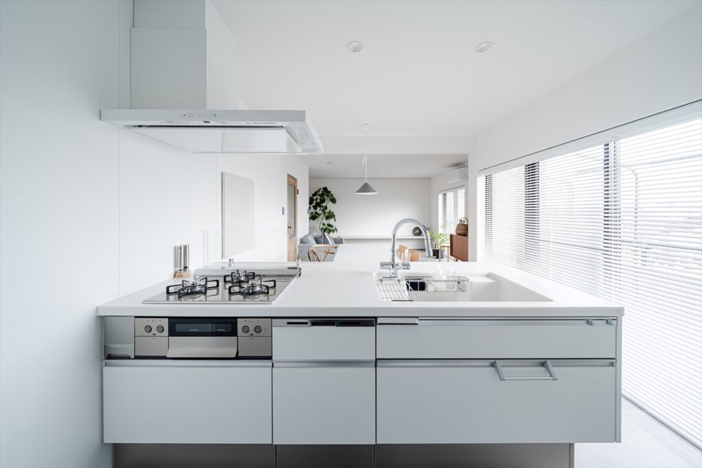Bright, modern kitchen with a white island, gas stovetop, and sink facing large windows with blinds in a daylight-filled space.