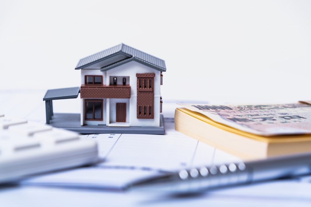 Model house placed on financial documents and money, illustrating real estate financing. (Toy house with papers and currency on a desk)