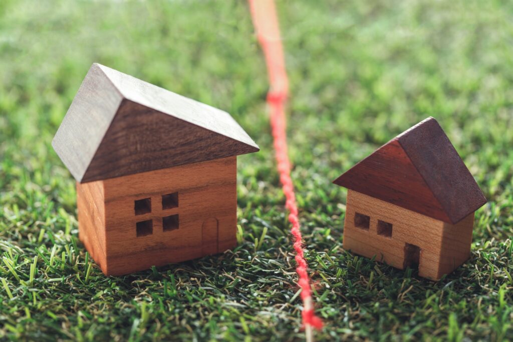 Two wooden toy houses on green grass with a red string running between them, like a playful outdoor setup.