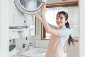 Smiling woman loading a front-loading washing machine in a bright laundry room.